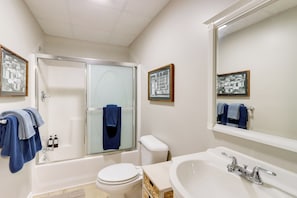 A bathroom with a bathtub, toilet, sink, and two framed pictures on the wall.