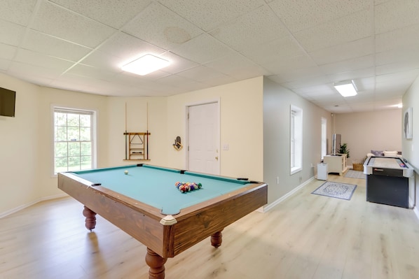 A pool table in a room with a door, windows, and a small kitchenette area.