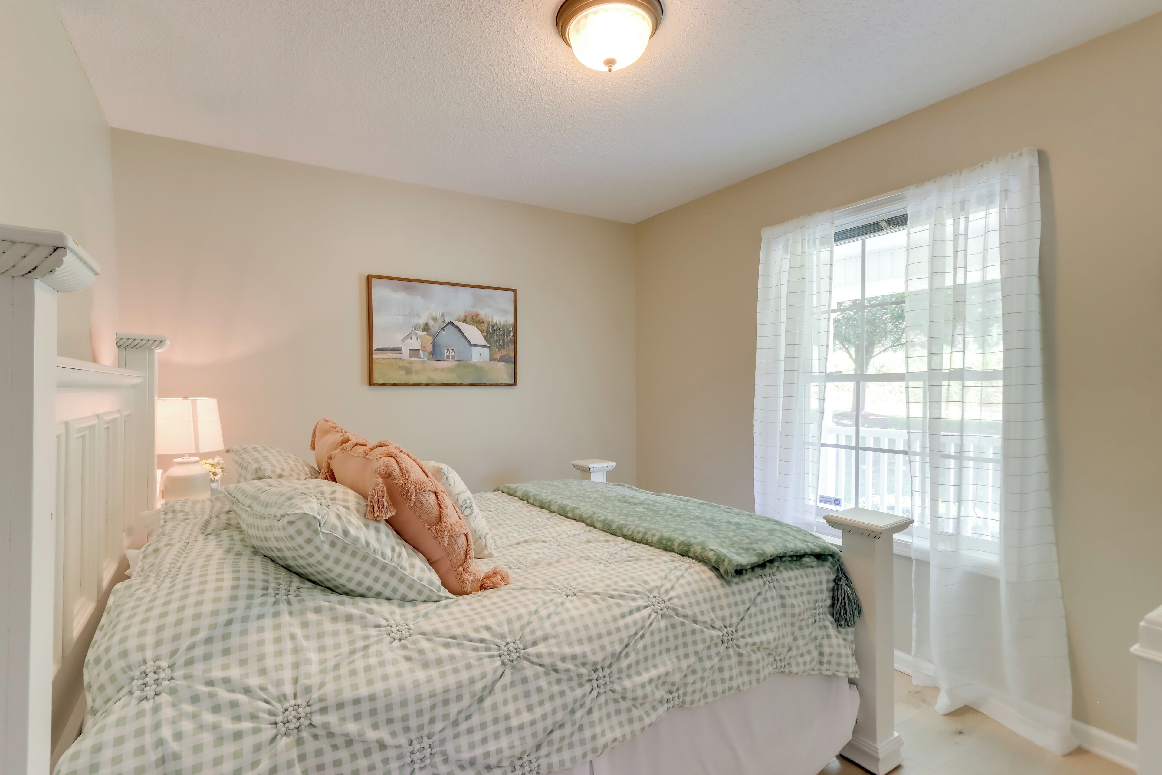 A bedroom with a bed, a window with curtains, a wall-mounted picture, and a bedside table.