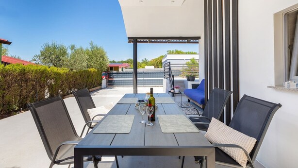 An outdoor patio with a table set for two, a bottle of wine, and a blue sofa. - Eco Beach House Corrine - 100 m from the Beach (Peroj)