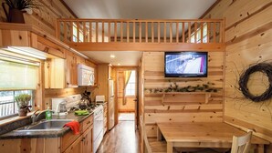 Een houten cabin met een keuken, eethoek en een televisie aan de muur.