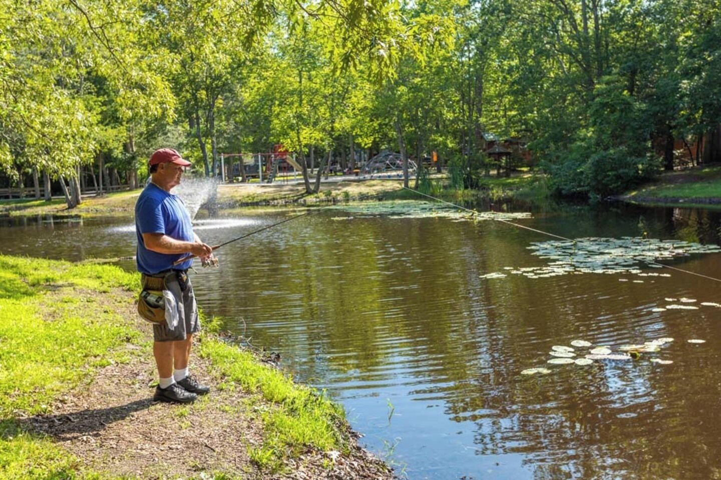 Un hombre pesca en un estanque tranquilo rodeado de abundante vegetación.
