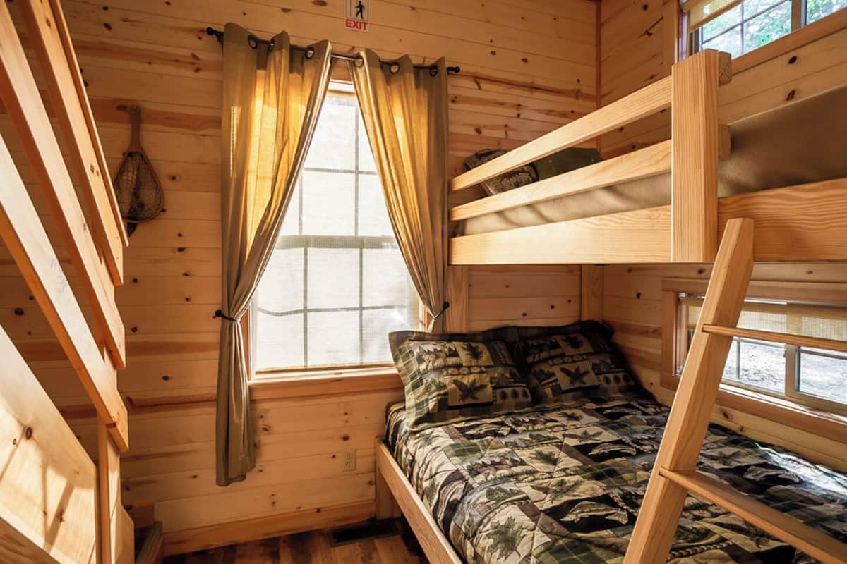 Una cabaña con literas, una ventana con cortinas y una escalera.
