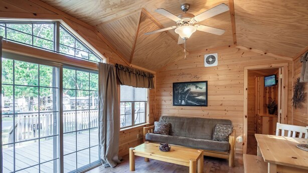 Een gezellig interieur van een chalet met een houten plafond, een plafondventilator, een bank, een salontafel en een eettafel.