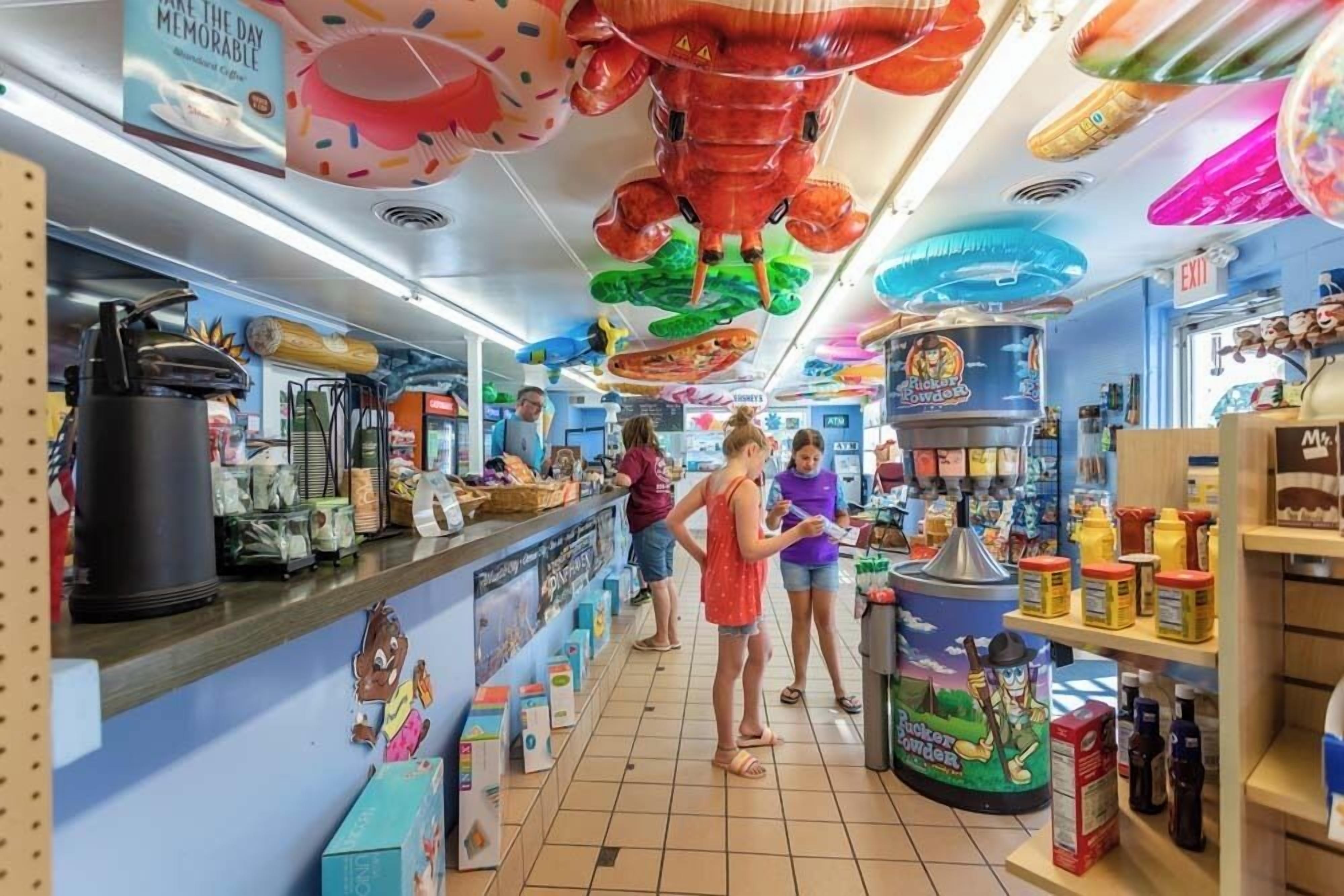 Una tienda luminosa con varios productos en estantes y adornos colgantes, incluyendo un cangrejo de gran tamaño y un personaje de un programa infantil.