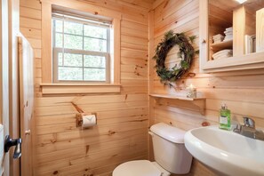 Un baño con paneles de madera, un inodoro, un lavabo y una ventana.