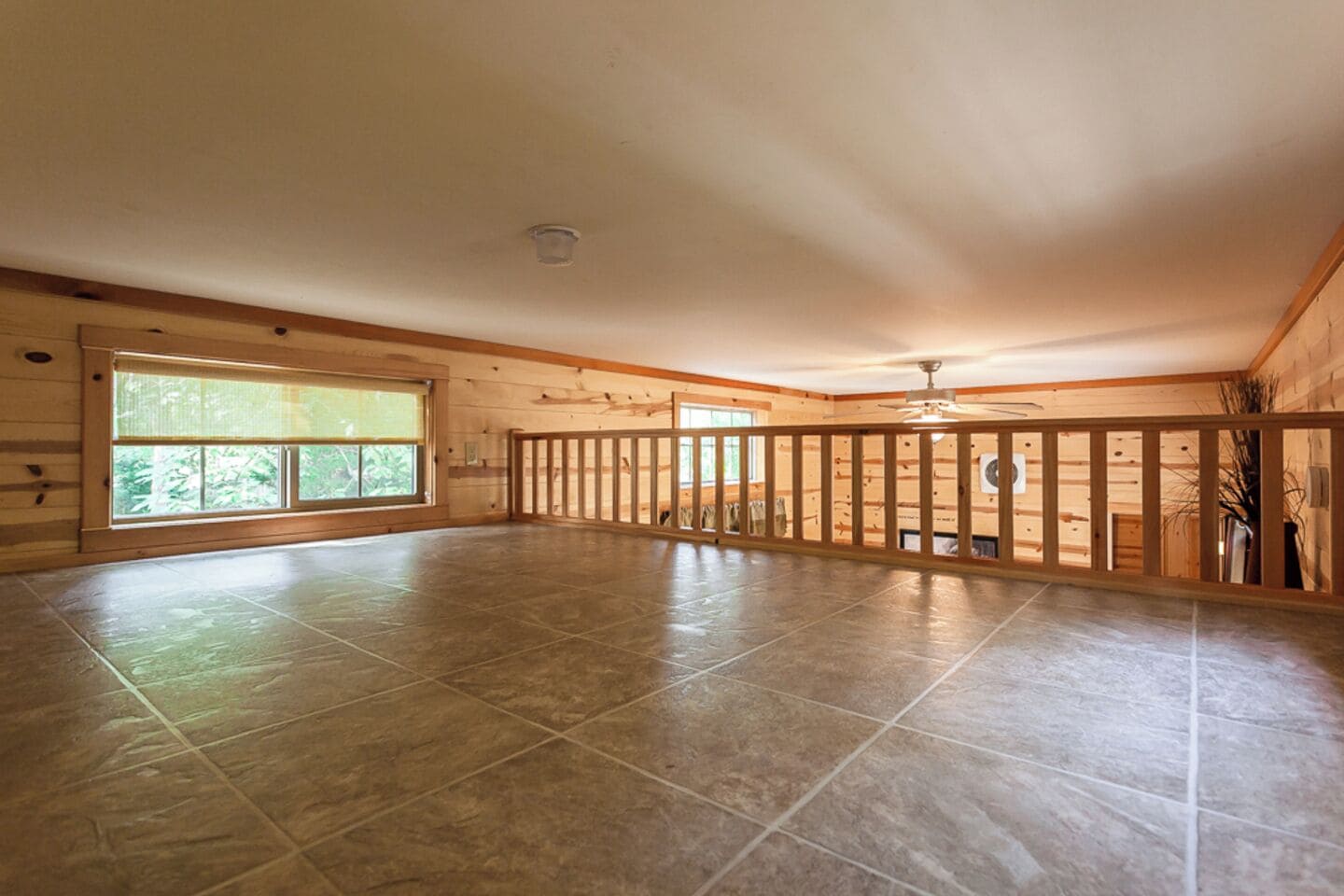 A spacious room with large windows, a wooden balcony, and a ceiling fan.
