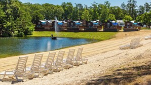 Een vakantiecomplex aan het meer met een rij strandstoelen, een fontein en bungalows met blauwe parasols.