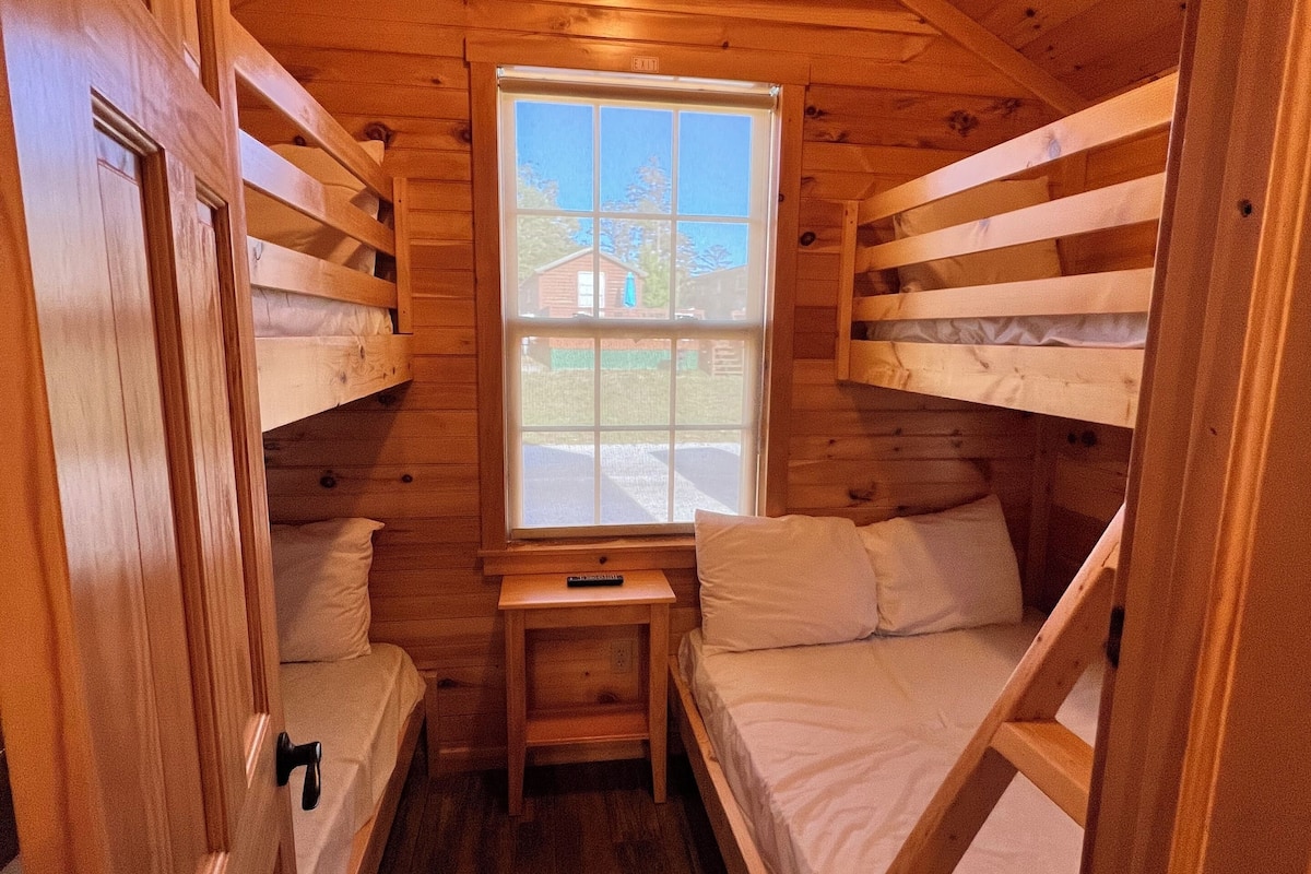 Una cabaña de paredes de madera y una ventana. Hay literas y una mesita.