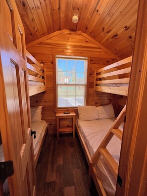 Una cabaña de paredes de madera y una ventana. Hay literas y una mesita.