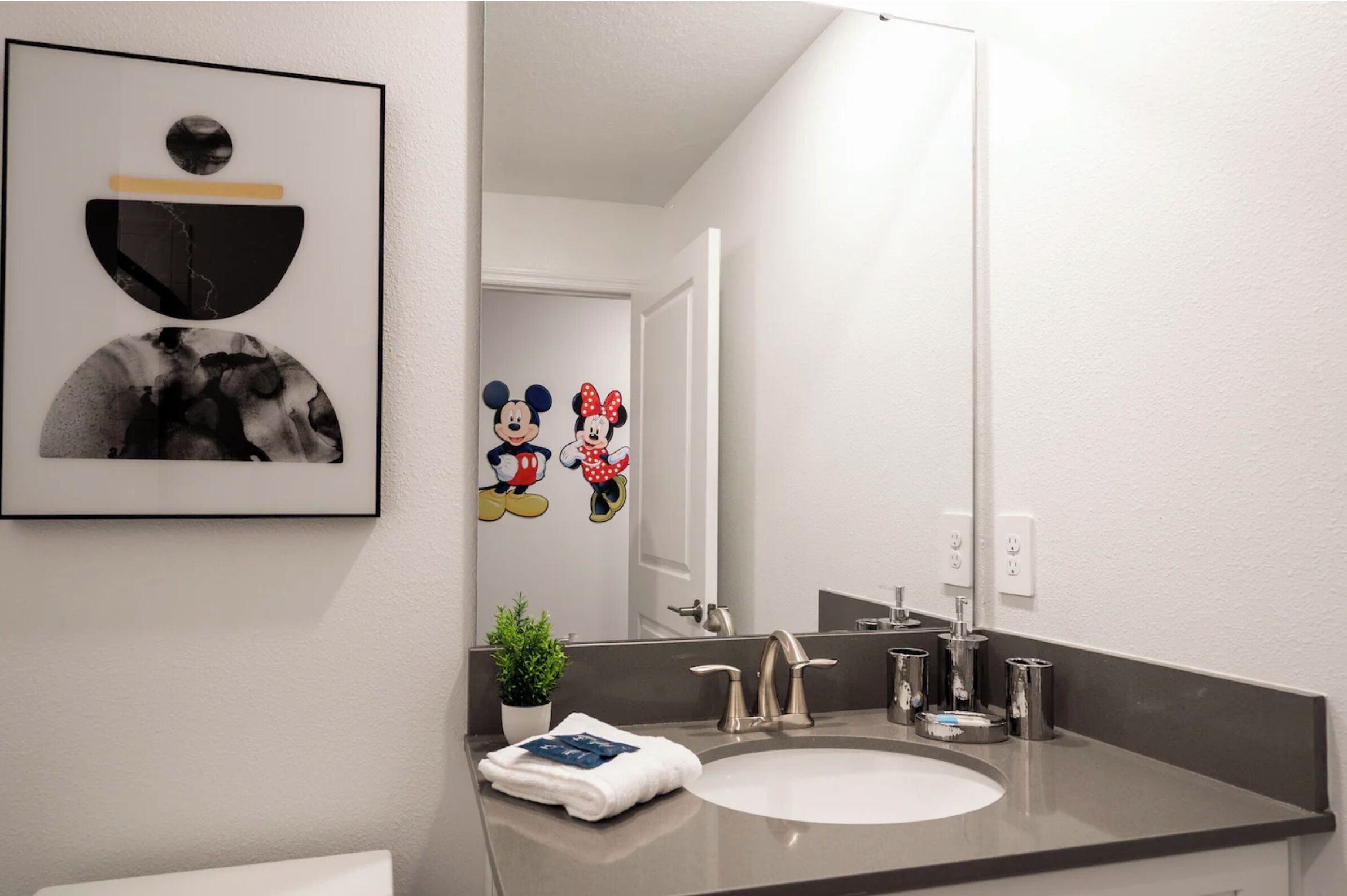 A modern bathroom with a large mirror, a sink, and a framed picture above it.