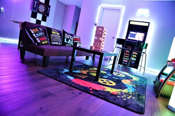 Une pièce avec un canapé, un jeu de fléchettes, une console de jeux et un tapis coloré.