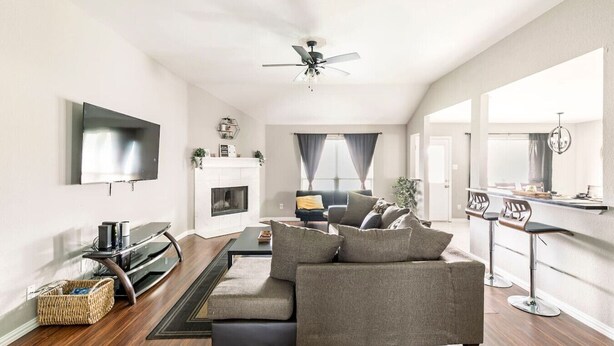 A modern living room with a fireplace, a sofa, a TV, and a dining area with bar stools.