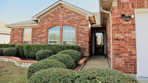 A brick house with a front entrance, a garage door, and a well-maintained hedge.