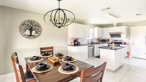 A modern kitchen with white cabinets, a central island, and a dining area with a wooden table and chairs.