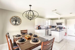 A modern kitchen with white cabinets, a central island, and a dining area with a wooden table and chairs. - Family Home| Large Patio| Game Room| AT&T Stadium (Arlington)