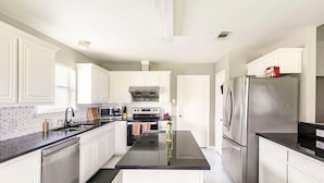 A modern kitchen with white cabinetry, a central island, stainless steel appliances, and a black countertop.
