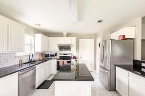 A modern kitchen with white cabinetry, a central island, stainless steel appliances, and a black countertop. - Family Home| Large Patio| Game Room| AT&T Stadium (Arlington)