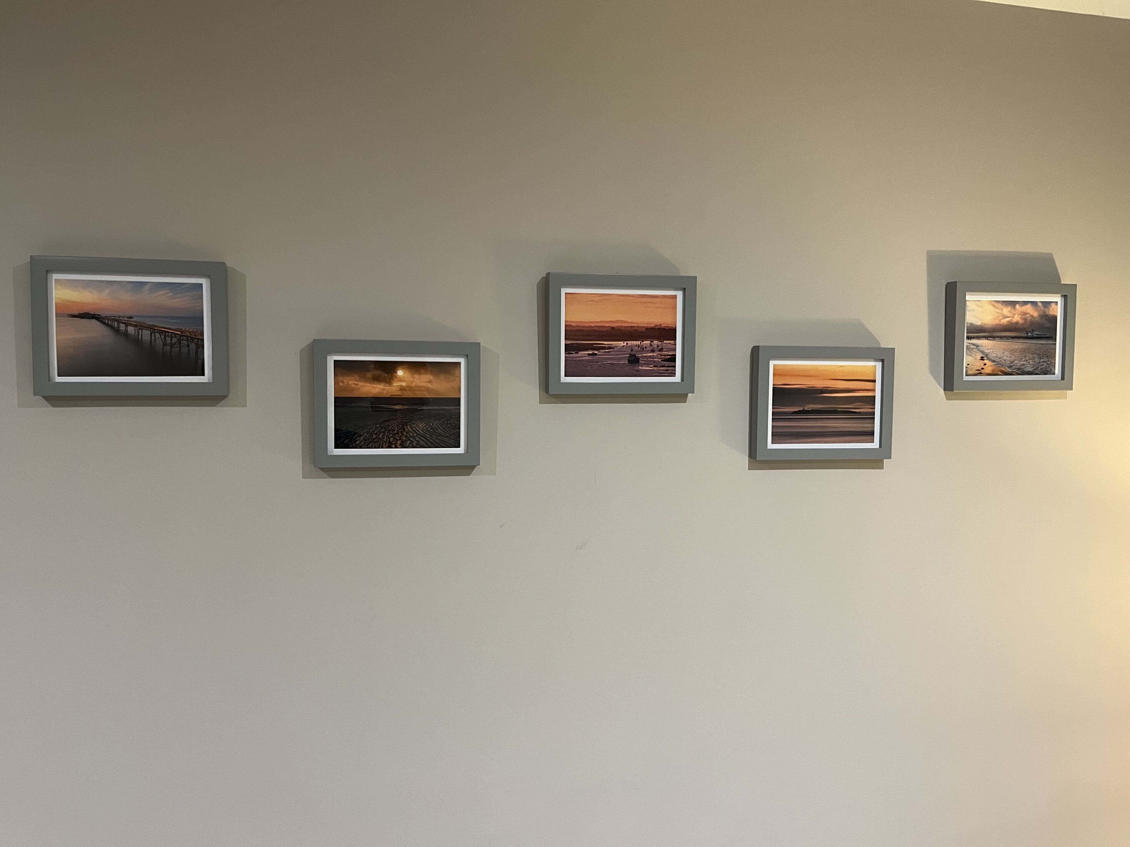 Un muro con cinque fotografie incorniciate di paesaggi costieri.