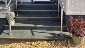 A modern entrance with a dark door, metal handrails, and a stone staircase leading to a porch area. - Secure, Detached bungalow overlooking Weston-super-Mare, the Severn and Wales (Hutton)