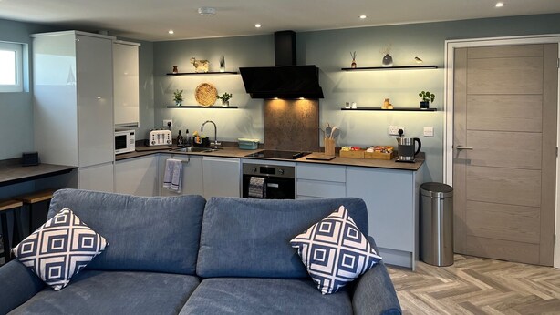A modern kitchen with a central island, built-in appliances, and decorative shelves. - Secure, Detached bungalow overlooking Weston-super-Mare, the Severn and Wales (Hutton)