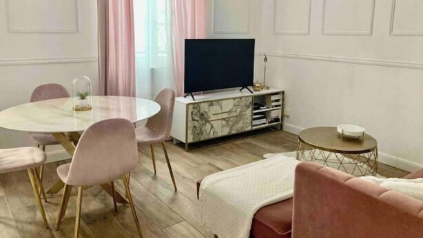 A modern living room with a round dining table, pink chairs, a flat-screen TV on a marble cabinet, a small side table, and a pink sofa. - Le Fuselier - Hyper Centre Cathédrale (Reims)