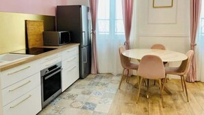 A compact kitchen with a microwave, oven, and refrigerator, a dining table with chairs, and a window with curtains. - Le Fuselier - Hyper Centre Cathédrale (Reims)