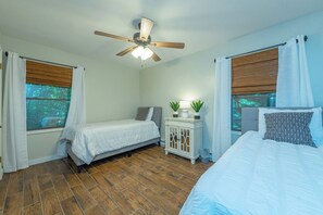 A bedroom with two beds, a ceiling fan, a nightstand with a lamp, and a window with curtains.