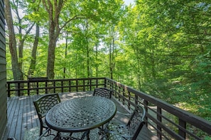 A wooden deck with a round table and chairs, surrounded by trees. - 2 mins to Ski! Hot Tub+Fire Pit, Fireplace, Grill! (Mars Hill)
