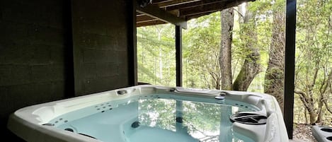 Uma banheira de hidromassagem em área externa coberta, com vista para árvores.