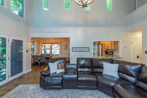 A spacious living room with a sectional sofa, a dining area, and a kitchen with a view of the outdoors.