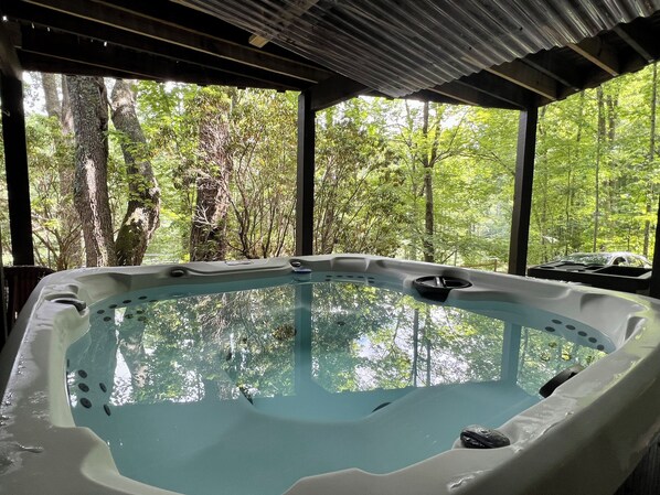A hot tub in a covered area with a view of a forest.