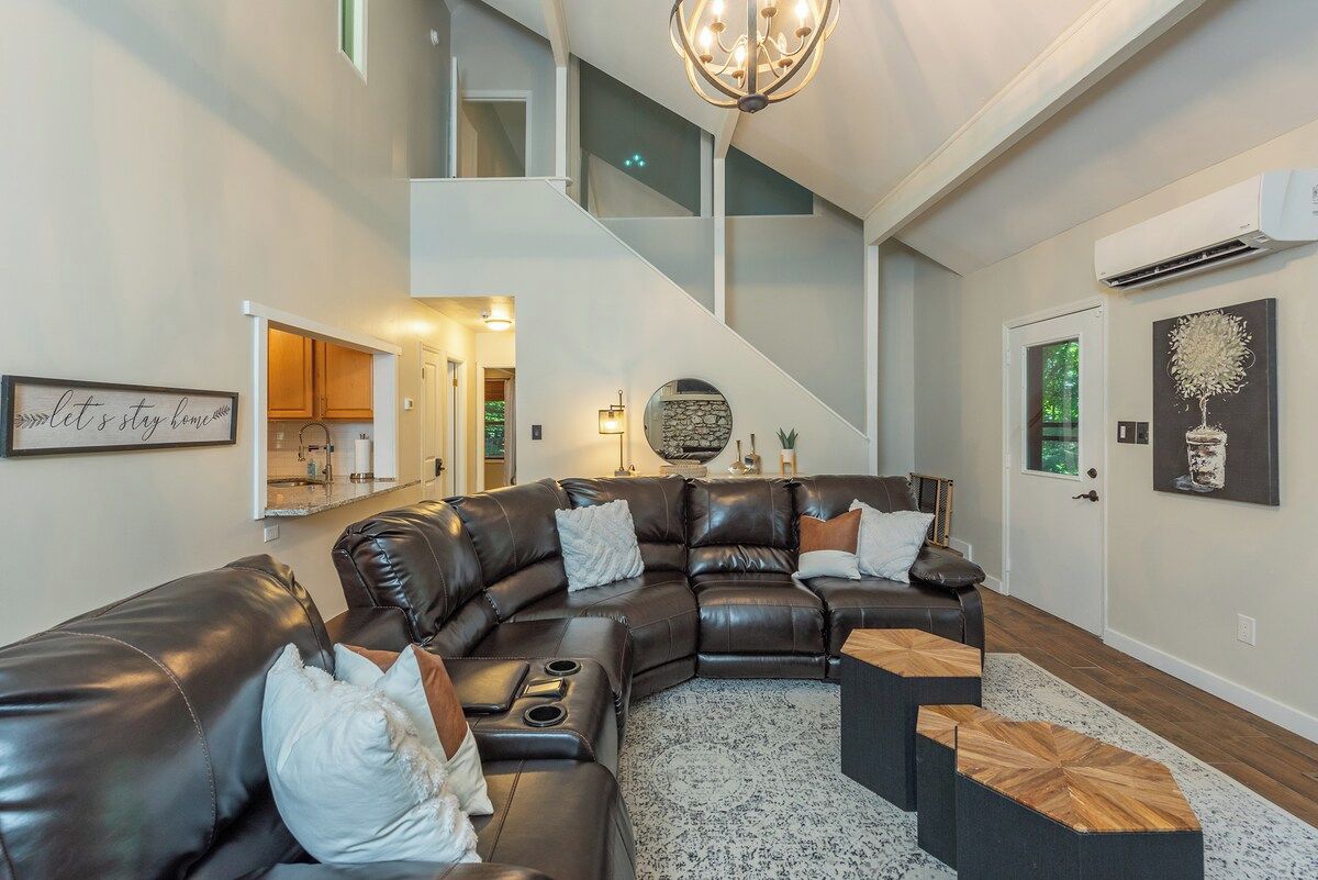 A modern living room with a sectional sofa, a staircase, and a kitchen in the background.