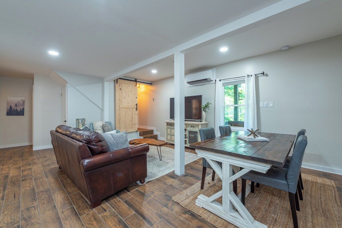 A modern living room with a brown leather sofa, a dining table with chairs, and a TV in the background.