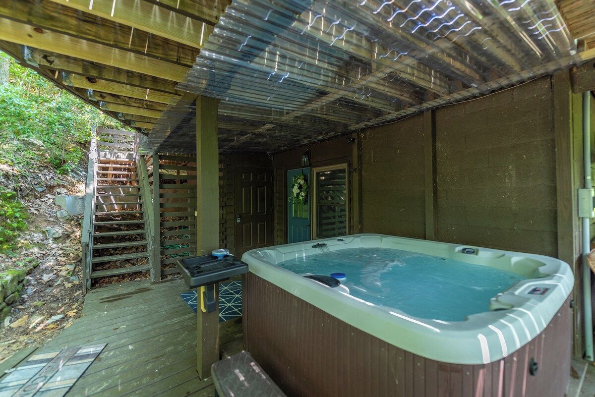 Un bain à remous sous une pergola en bois, avec une terrasse en bois et un mur de briques en arrière-plan.