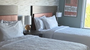 A hotel room with two beds, a nightstand with a lamp, a framed picture on the wall, and a window with a view. - Home2 Suites By Hilton Racine (Sturtevant)