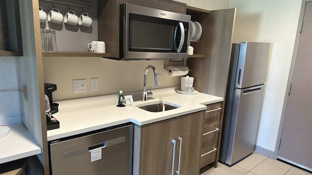 A modern kitchen with a built-in microwave, stainless steel refrigerator, and a dishwasher. - Home2 Suites By Hilton Racine (Sturtevant)