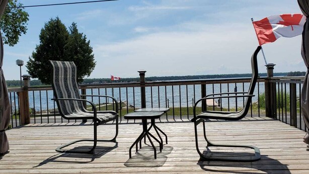 A wooden deck with metal chairs and a table, overlooking a body of water with a flag.