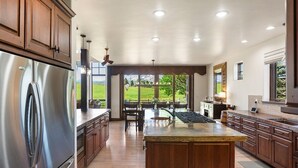 A spacious kitchen with a large island, stainless steel appliances, and a view of a green landscape.