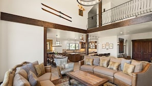 A spacious living area with a large sofa set, a wooden coffee table, and a dining table with chairs. A kitchen is visible in the background, and there is a balcony with a railing.