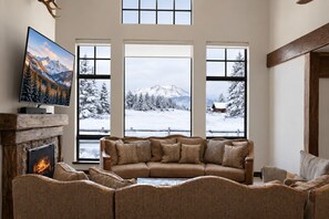 Una sala de estar acogedora con chimenea, un ventanal con vistas a una montaña nevada y un televisor sobre una repisa de madera.