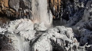 Une cascade gelée, ornée de stalactites et de rochers recouverts de neige.
