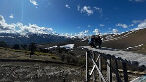 Une terrasse en bois surplombant un paysage montagneux, avec des zones enneigées et un ciel dégagé.