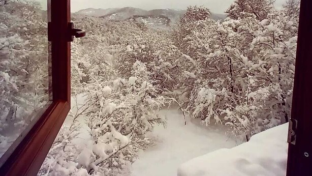 Un paysage enneigé, vu à travers une fenêtre ouverte.