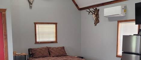 A bedroom with a bed, a ceiling fan, a wall-mounted TV, a refrigerator, and a large bull skull decoration.