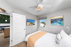 Une chambre à coucher avec un lit, un ventilateur de plafond, une fenêtre et des œuvres d’art accrochées aux murs.