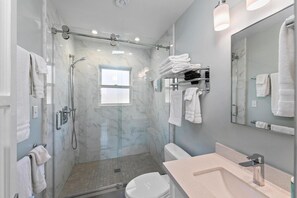 A modern bathroom with a glass-enclosed shower, a toilet, a sink, and a large mirror.