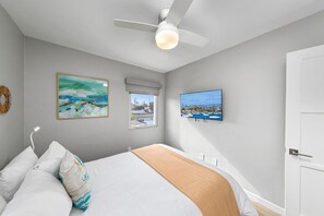Une chambre à coucher avec un lit, un ventilateur de plafond, une télévision et deux tableaux.