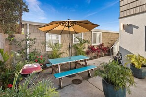 A patio with a blue table and bench, a beige umbrella, and various potted plants.