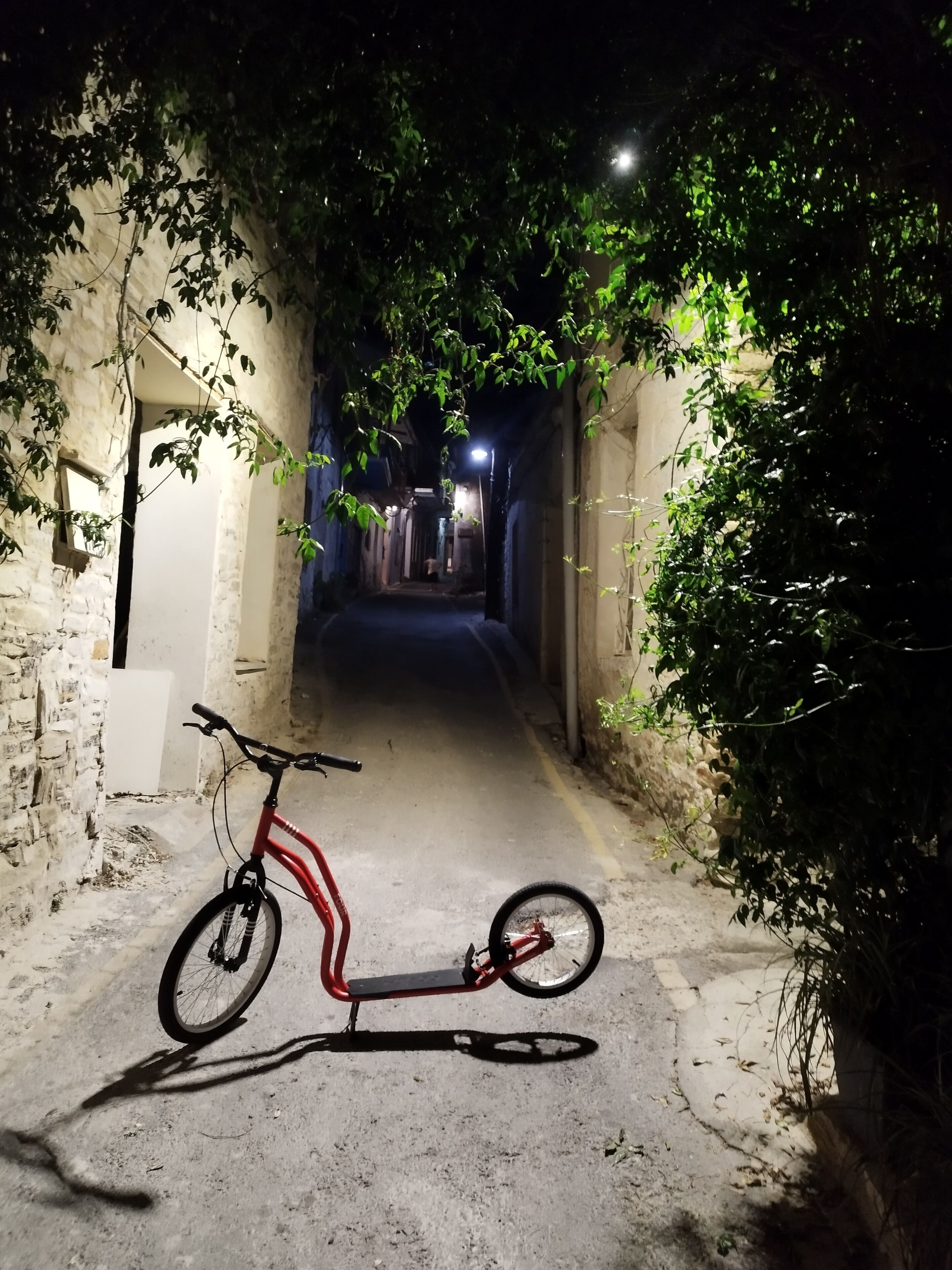 A narrow alleyway with a red electric scooter parked on the left.